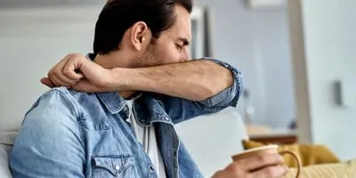 man coughing into his elbow while drinking tea