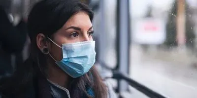 Woman on a bus looking out of window, wearing a face mask