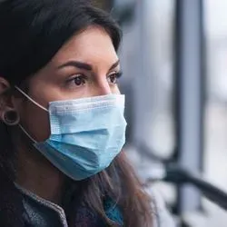 Woman on a bus looking out of window, wearing a face mask