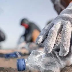 Person picking up a plastic bottle on a beach
