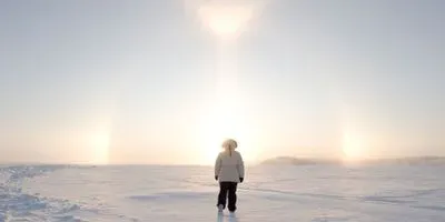 Person walking in the arctic towards the sun