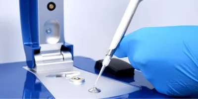 A gloved hand dropping a sample on a microscope in a lab.
