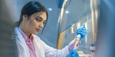 A scientist in a lab working under a biosafety cabinet.
