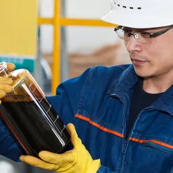 Man in hard hat and gloves holds a glass bottle of dark liquid
