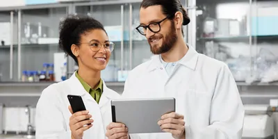 A Black woman with her hair up holds a phone while a white man with his hair pulled back holds a tablet.
