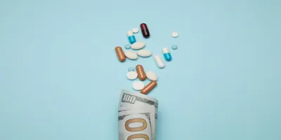 A $100 bill and a handful of colorful pills on a blue background
