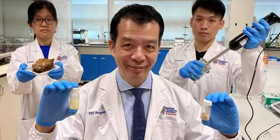 Three scientists in white lab coats and blue gloves hold up various lab instruments and mayonnaise that has been made with their plant-based product.
