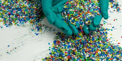 gloved hand holding small, colored pieces of plastics