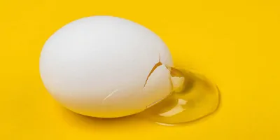 A cracked egg with egg white leaking out on a yellow table