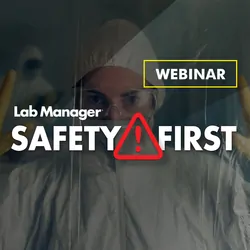 Person in a white hazmat suit, protected with yellow gloves and goggles, behind a restricted area