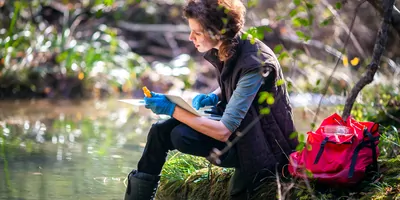 Female researcher beside a stream taking samples