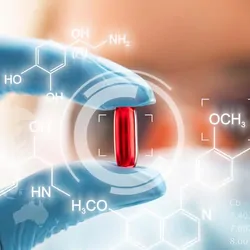 Women researcher, wearing gloves, holding a gel pill in her fingers up to her eye