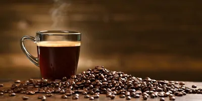 Glass cup with coffee in it next to some coffee beans on a wood table