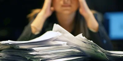 stack of papers in front of a person looking tired in the background