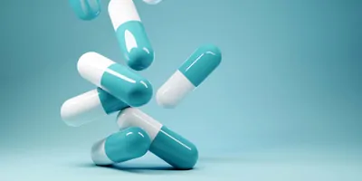 Blue and white pills falling onto a light ble table with ligth blue background