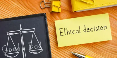 A chalk board with scales drawn on it next to a note pad with the words "ethical decision"