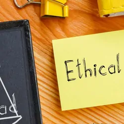 A chalk board with scales drawn on it next to a note pad with the words "ethical decision"