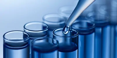 A picture of the end of a pipette pipetting water into a glass container.