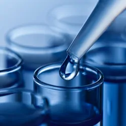 A picture of the end of a pipette pipetting water into a glass container.