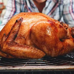 A cooked turkey being pulled from the oven