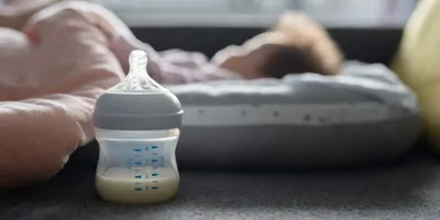 Baby bottle with milk in it next to a small bed with a baby in it
