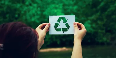 Woman holding a paper sheet with recycle symbol over green forest nature background. Ecology and greening concept.