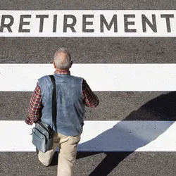Older man crossing a crosswalk with the word "retirement" written on it