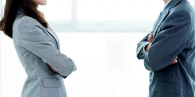 Two coworkers in suits facing each other, arms crossed