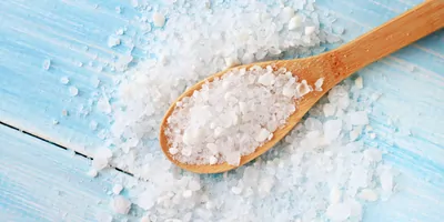 A wooden spoon filled with table salt, resting on a blue table