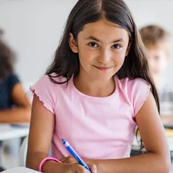 A portrait of small happy school girl sitting at the desk in classroom, looking at camera