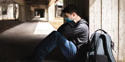 Student wearing mask looking stressed sitting on the floor