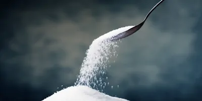 A spoon full of white sugar being poured into a pile
