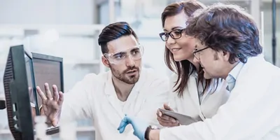 Three scientists discuss information displayed on a computer screen.