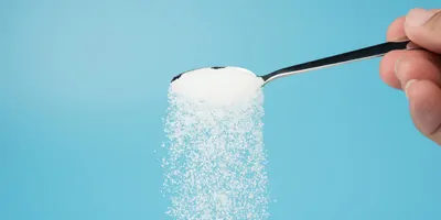 Sugar pouring out of a spoon on a blue background