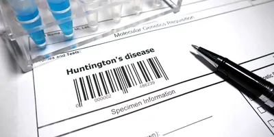 Paper with pen and test tubes resting on it, with the words huntingtons disease written on the page