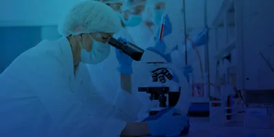 Laboratory researcher dressed on PPE looking through a microscope
