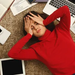 Exhausted student girl lying on the floor among textbooks, tests and gadgets