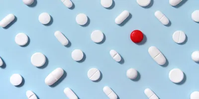 White pills arrangement on soft blue background with one red pill standing out from them