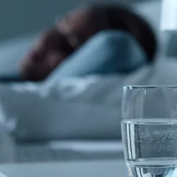 Women, out of focus, sleeping in bed at night with glass of water in the foreground