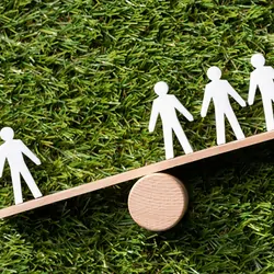 People cutouts on an imbalanced seesaw on a grassy background