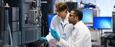 Two technicians working together at an LC-MS equipment bank in a lab.