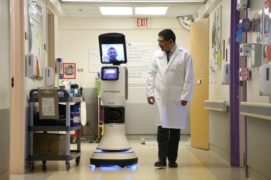 Physician walks alongside a telemedicine robot down a hospital hallway Physician walks alongside a telemedicine robot down a hospital hallway