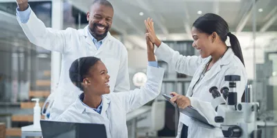 Shot of a group of young scientists giving each other a high five while using a laptop in a laboratory