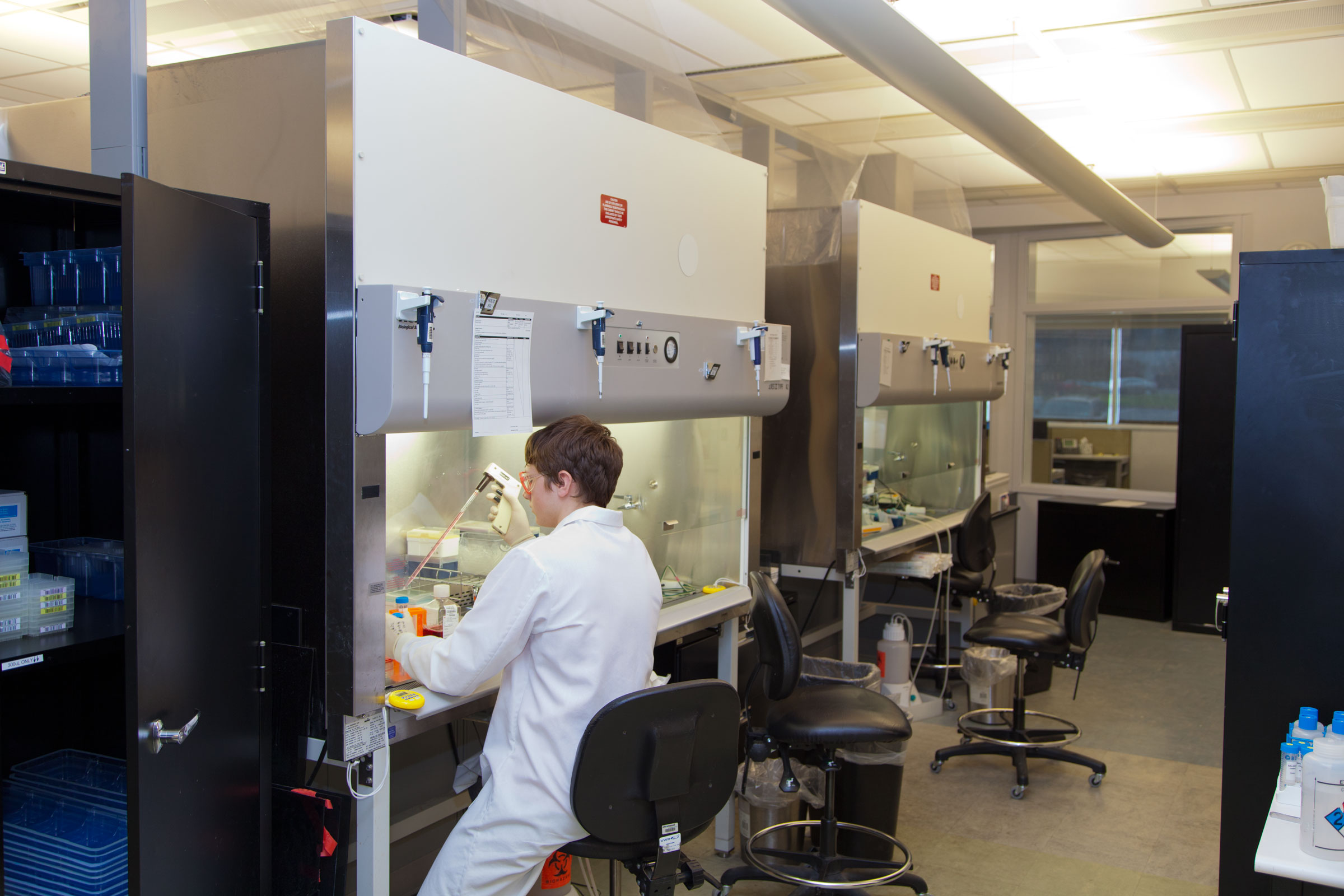A scientist uses a manual pipette in a hood