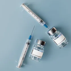 Two syringes and vaccine vials lay on a gray table