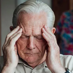 Elderly man rubs his temples while his wife looks on with concern