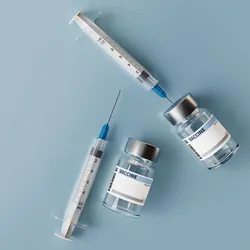 Syringes lie next to vaccine vials on a blue table