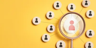 image of a magnifying glass held over a number of wooden pegs with silhouettes of people on them suggestive of the idea of finding the right candidates when hiring