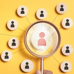 image of a magnifying glass held over a number of wooden pegs with silhouettes of people on them suggestive of the idea of finding the right candidates when hiring