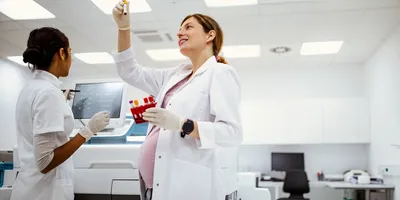 a pregnant lab technician hold up a vial illustrating the importance of saelty when working with reproductive hazards